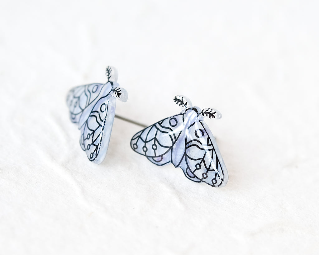 two clear butterfly-shaped earrings with intricate black and white designs.
