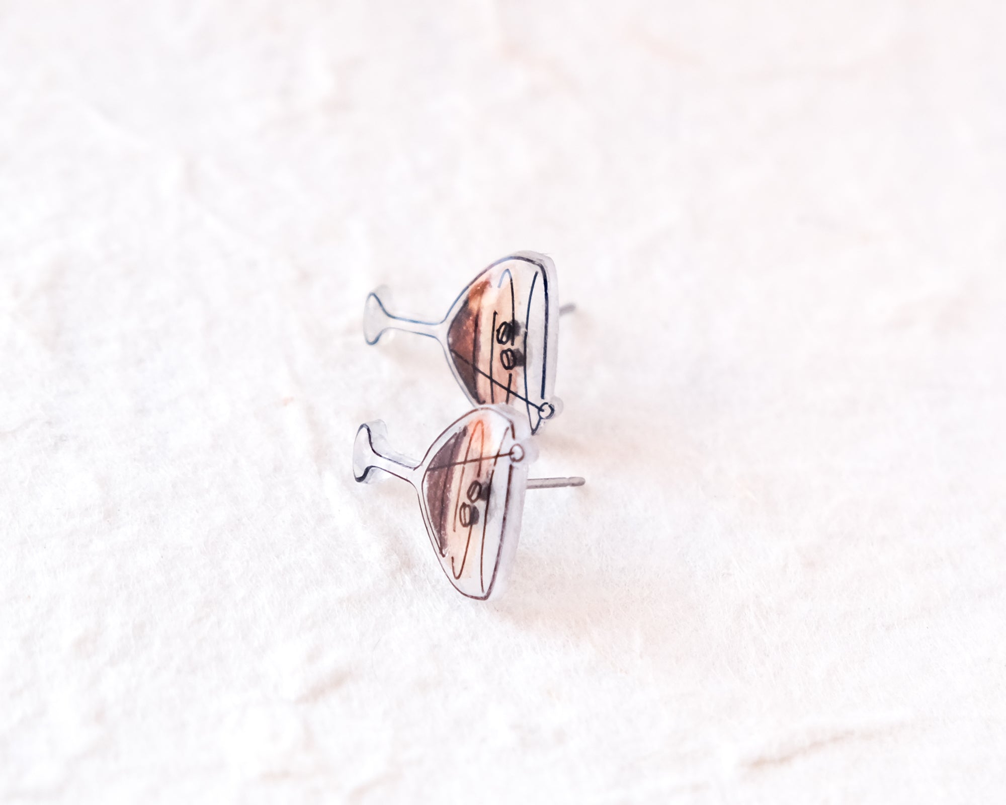 A pair of silver earrings with a cocktail glass design, placed on a white surface.