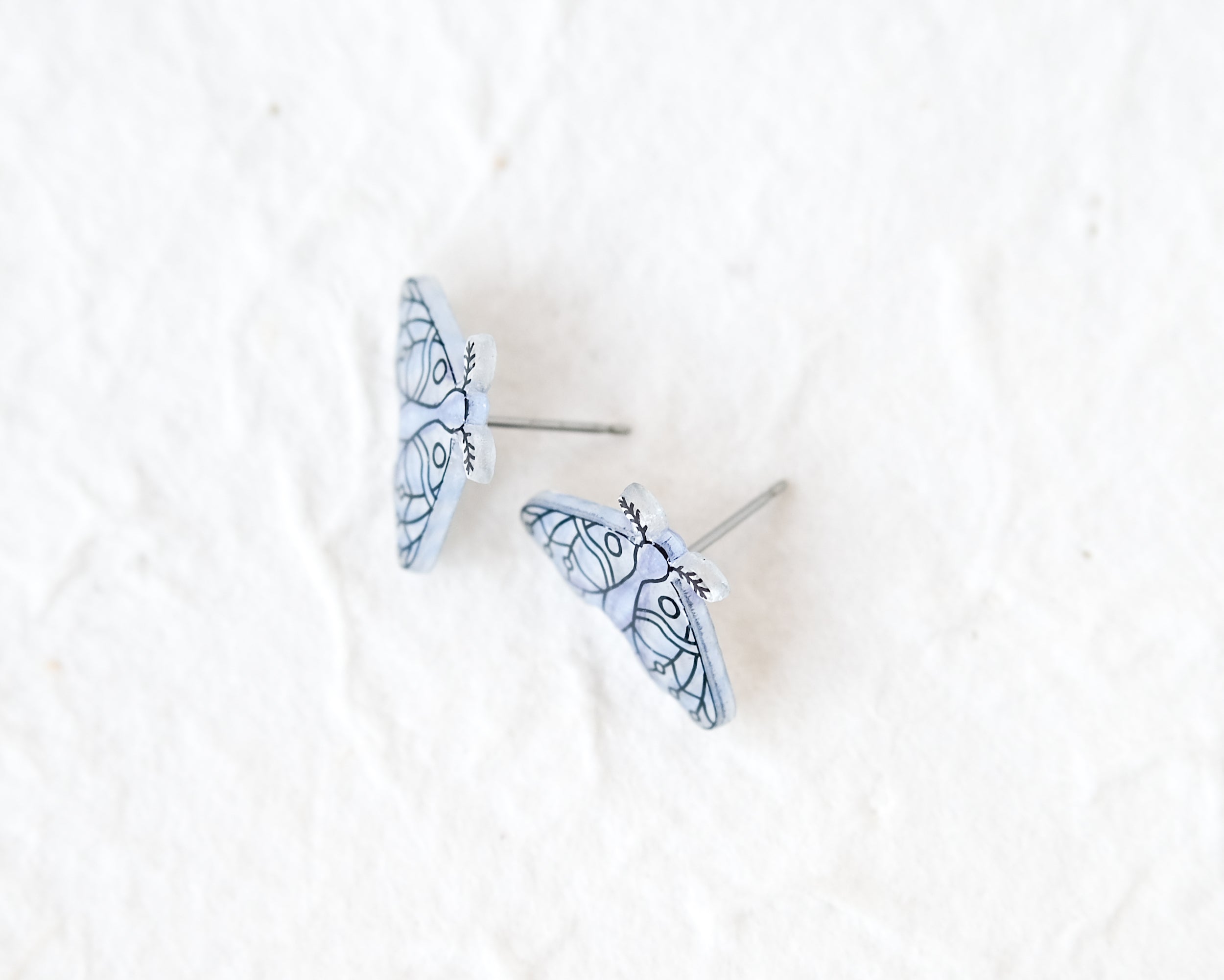 A pair of blue butterfly-shaped earrings with intricate designs on a white background.