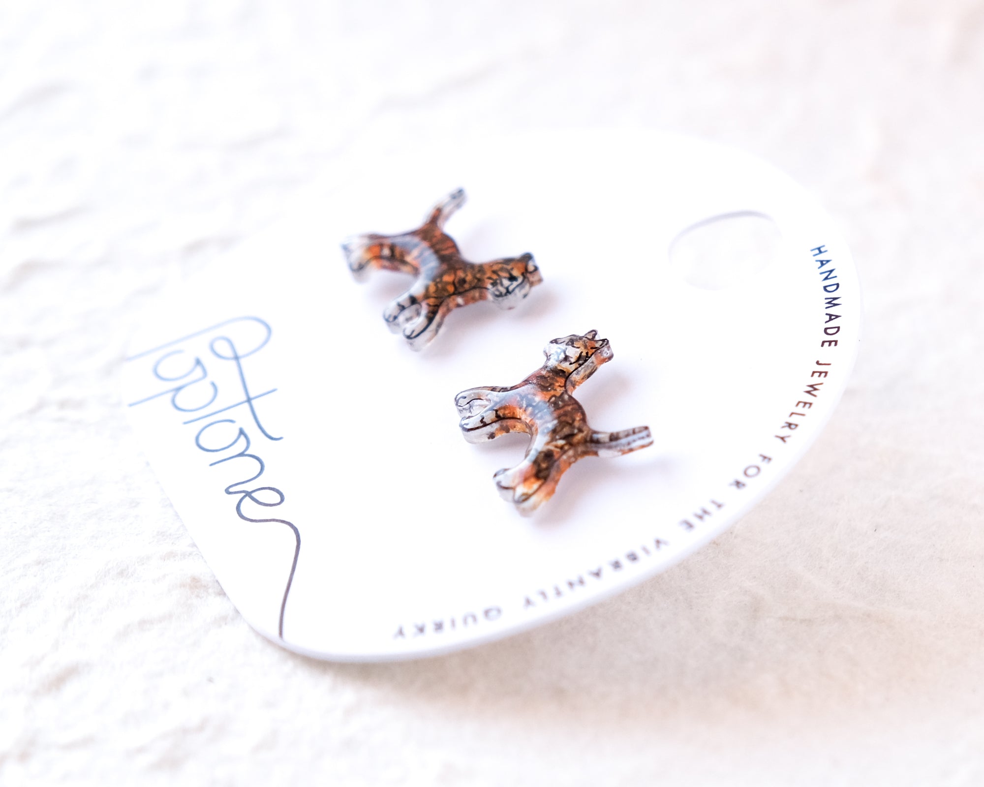 a pair of earrings with a unique design, placed on a white circular tag that has text printed on it.