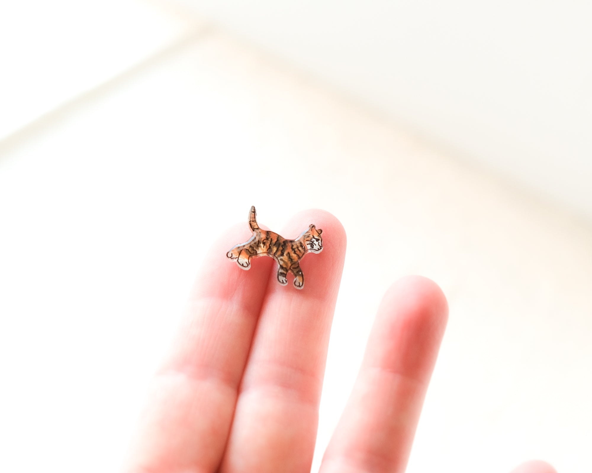 A small, colorful cat figurine is being held in a person's hand against a white background.