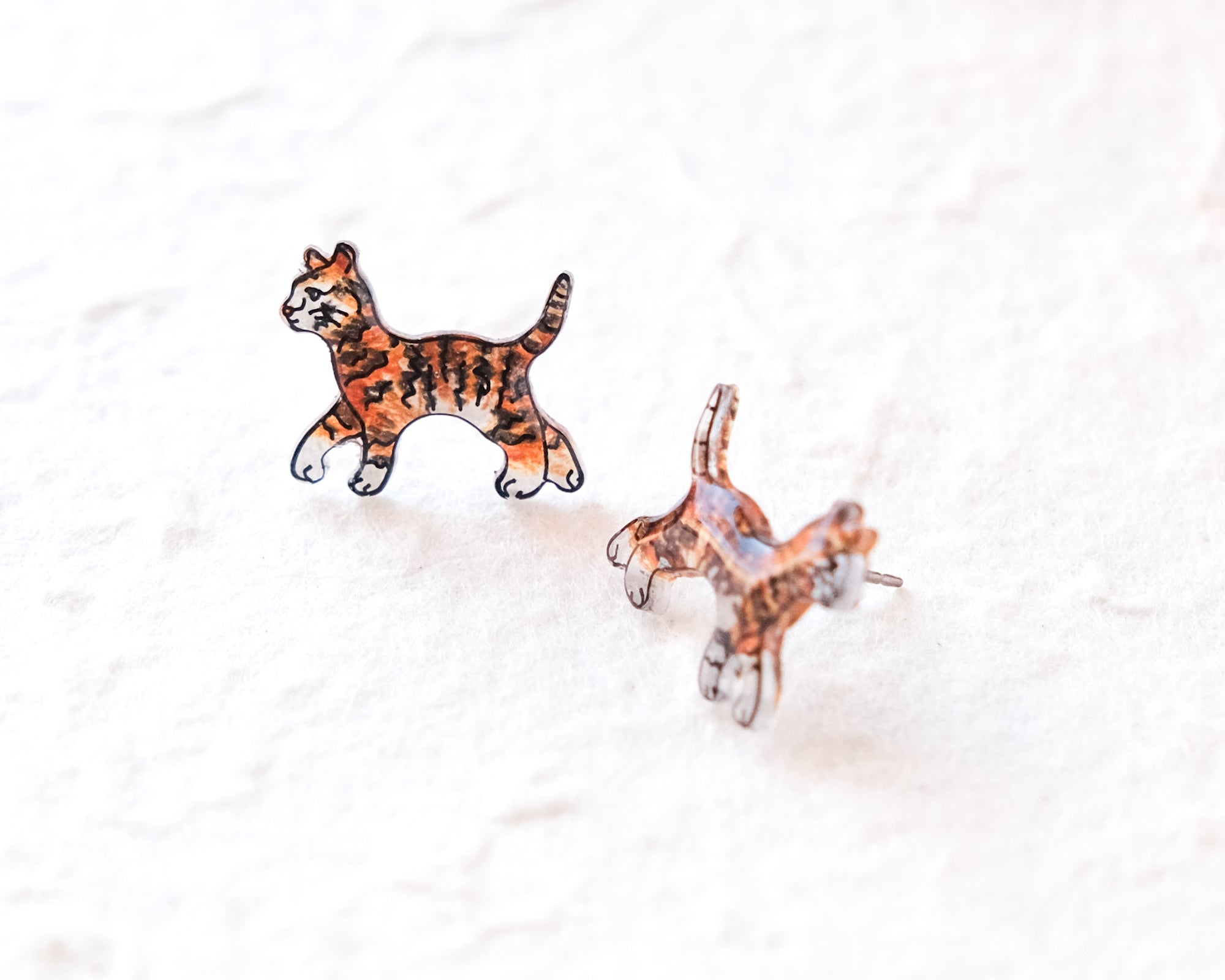 two cat-shaped earrings on a white surface.