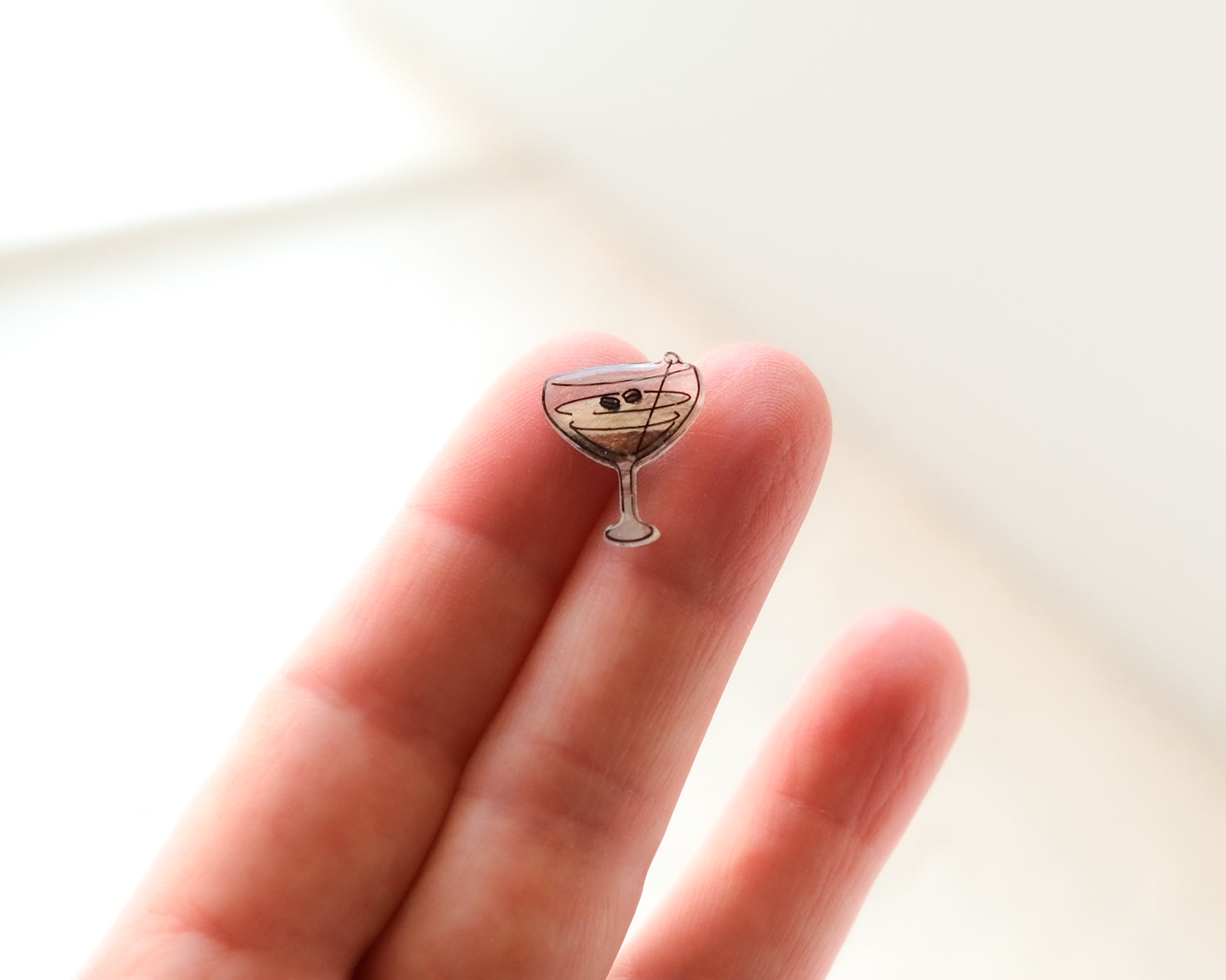 A small pin or badge in the shape of a martini glass with a straw is being held in a person's hand.