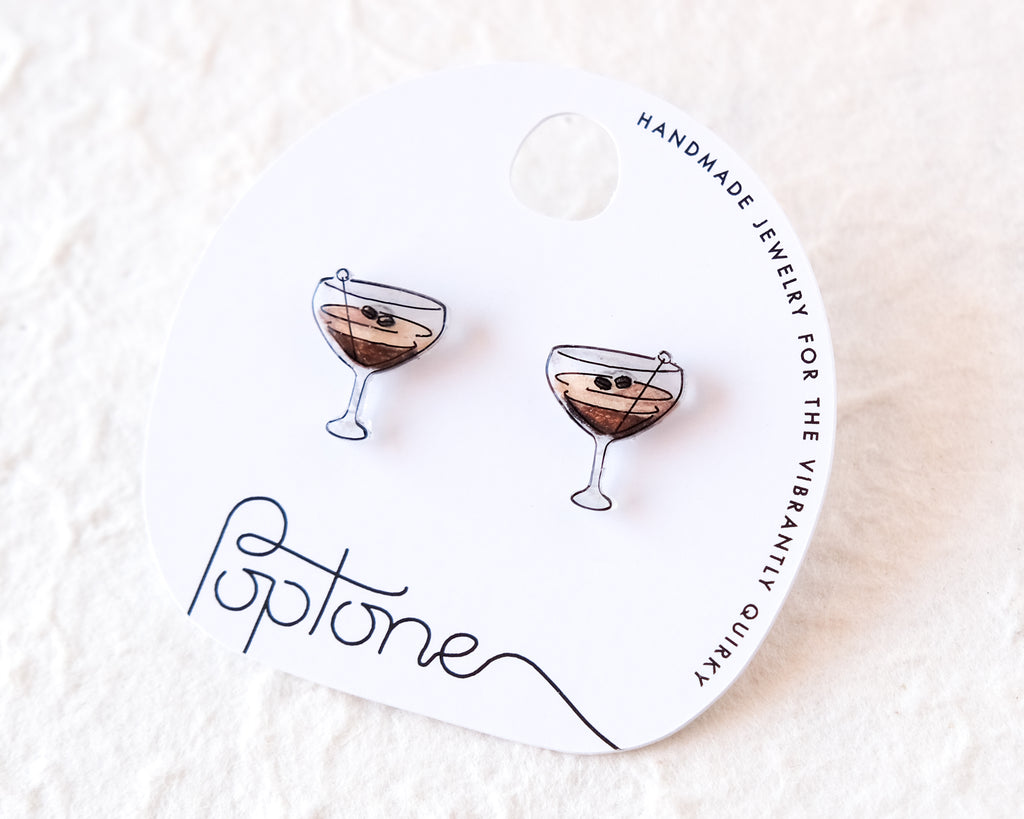 a pair of earrings with a design of two martini glasses, each containing a small black object, placed on a white background.