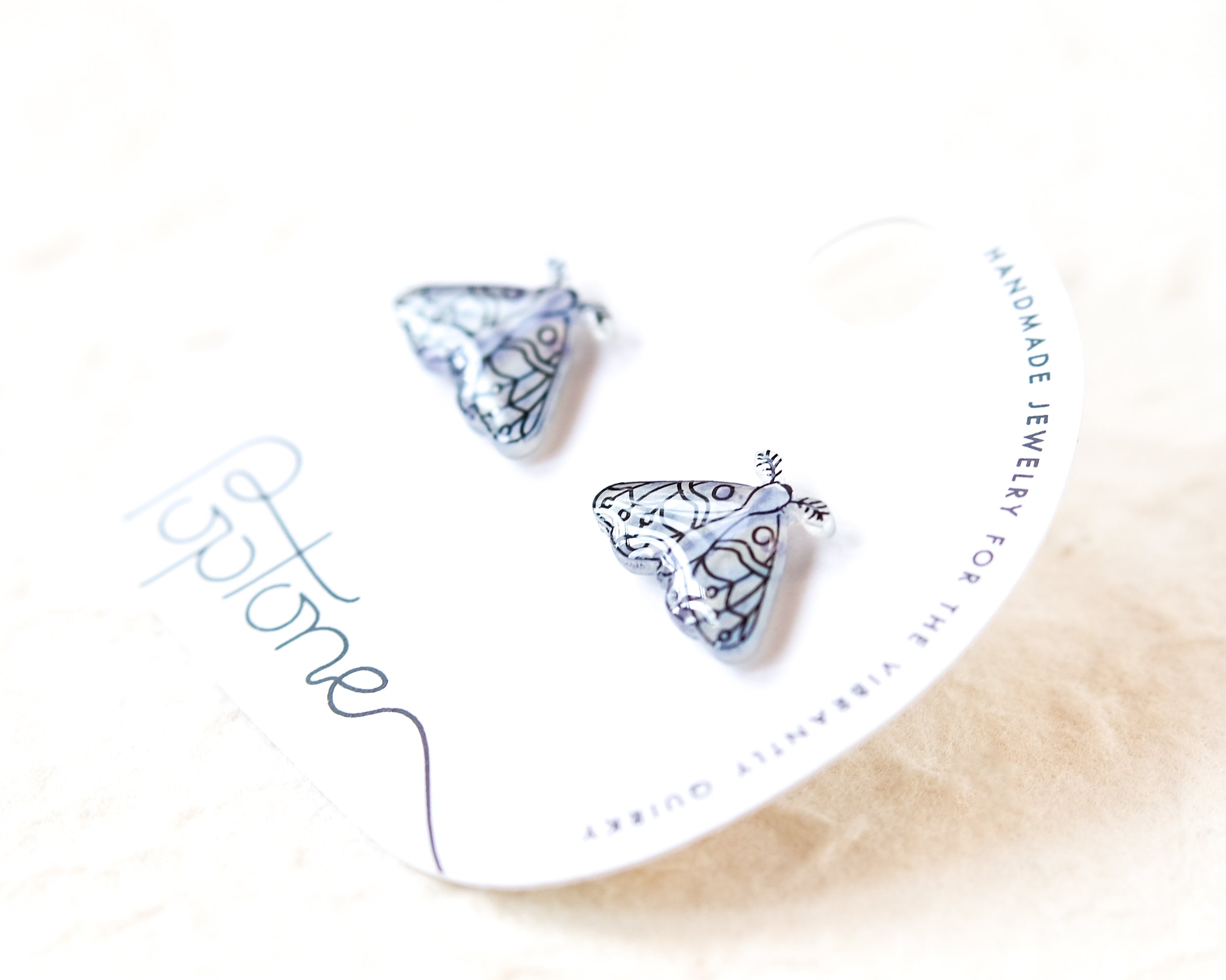 a pair of silver earrings with a butterfly design, placed on a white card with text.