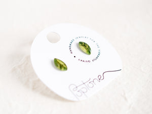 a pair of green leaf earrings sitting on top of a white plate