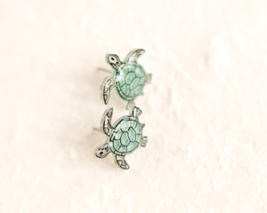 a pair of sea turtle earrings sitting on top of a white surface