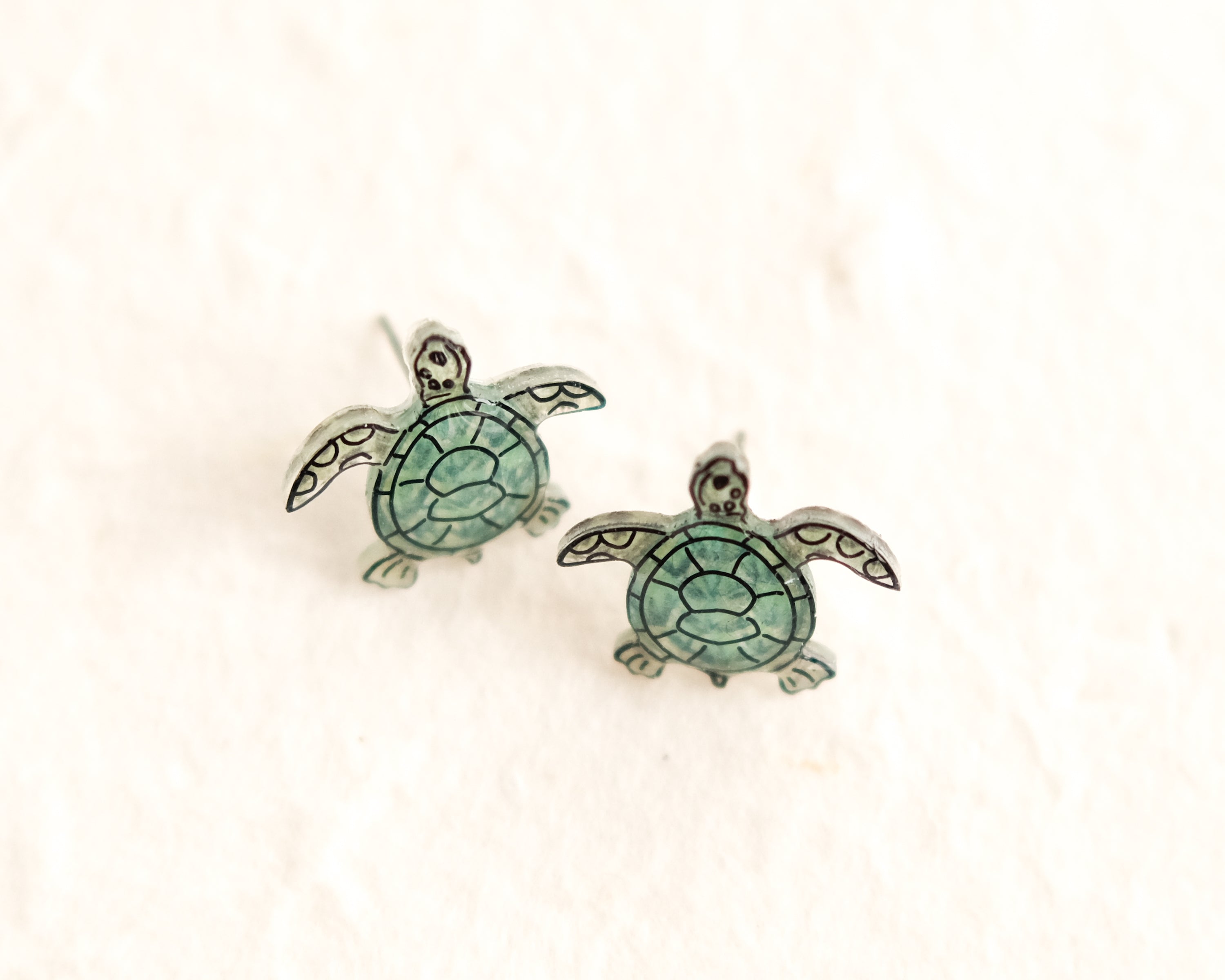 a pair of sea turtle earrings sitting on top of a white surface