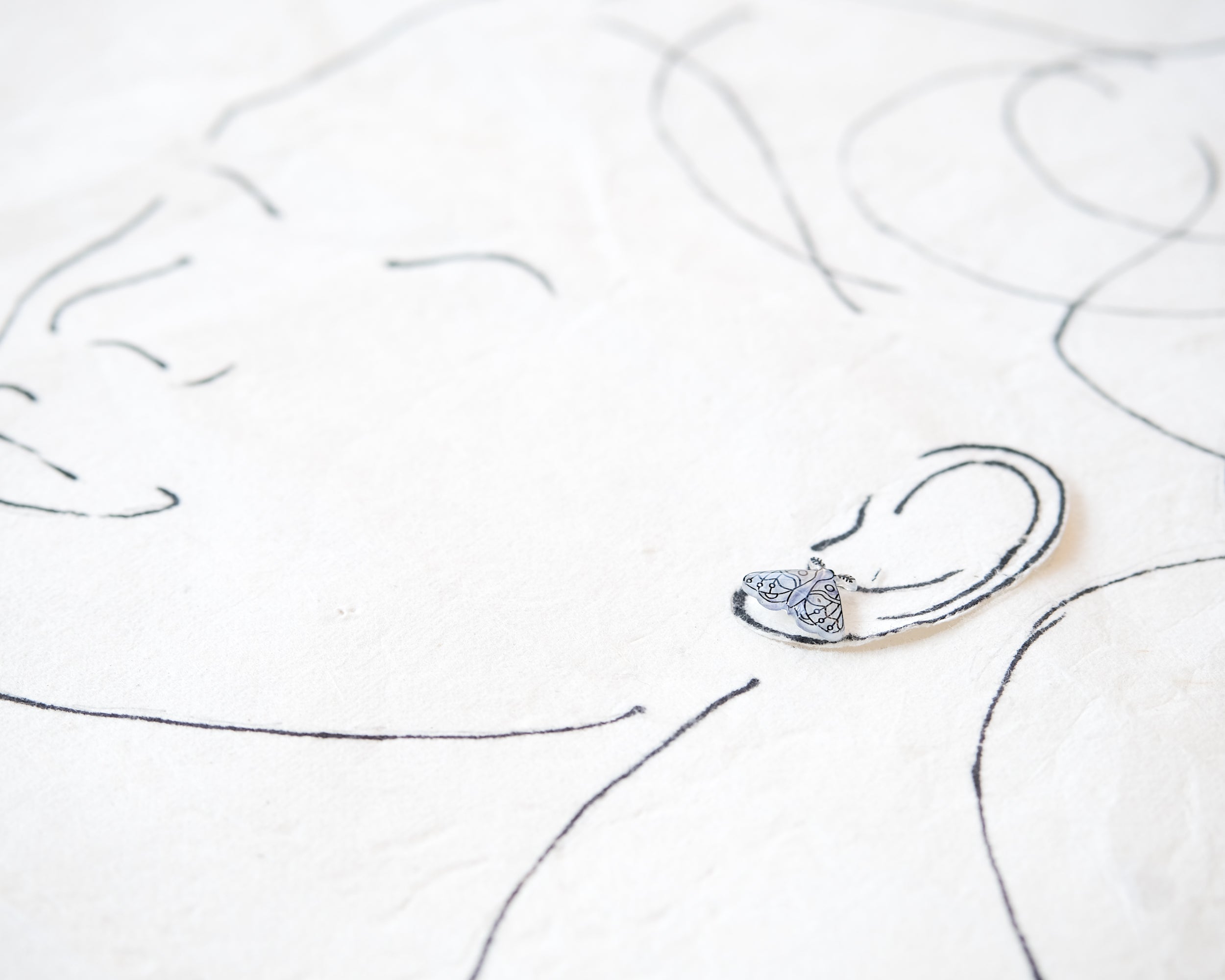 a silver earring with a butterfly design, placed on a white surface with a simple black line drawing of a face.