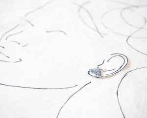 a silver earring with a butterfly design, placed on a white surface with a simple black line drawing of a face.