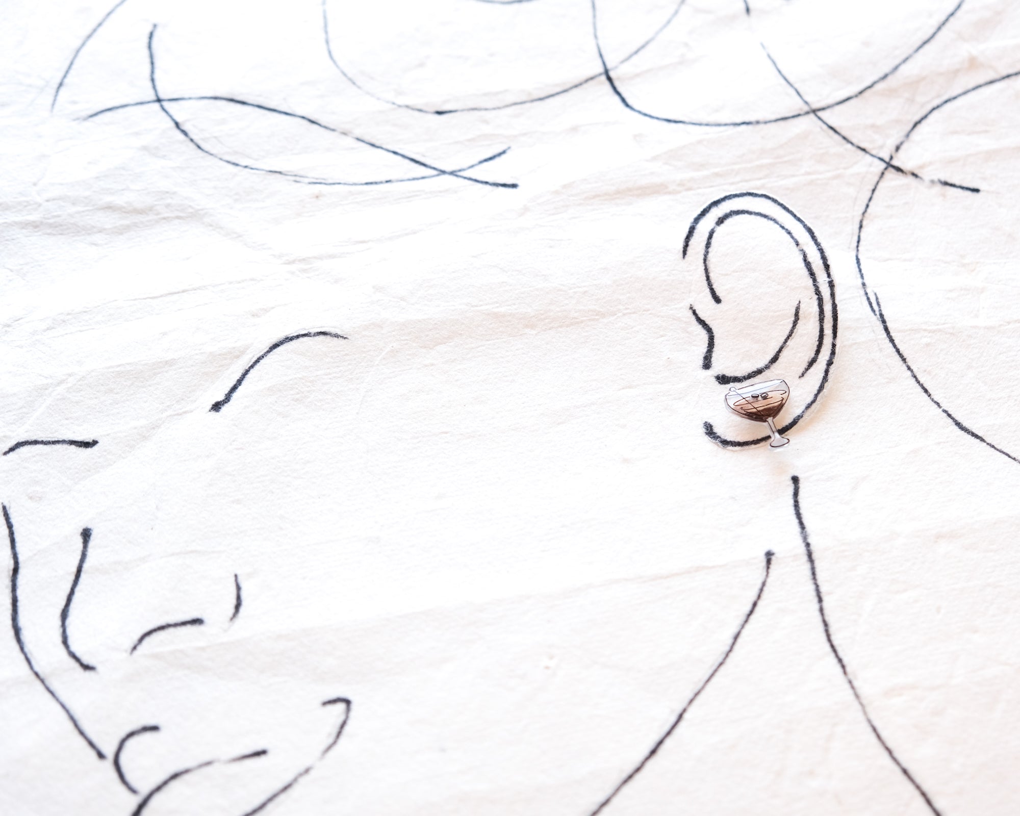 a close-up view of a pair of earrings, with the earrings being the main focus. The earrings are positioned in the center of the image, drawing attention to them. The background is a white fabric with black lines, which adds depth and texture to the image. The overall composition is simple and minimalistic, with the earrings being the focal point.
