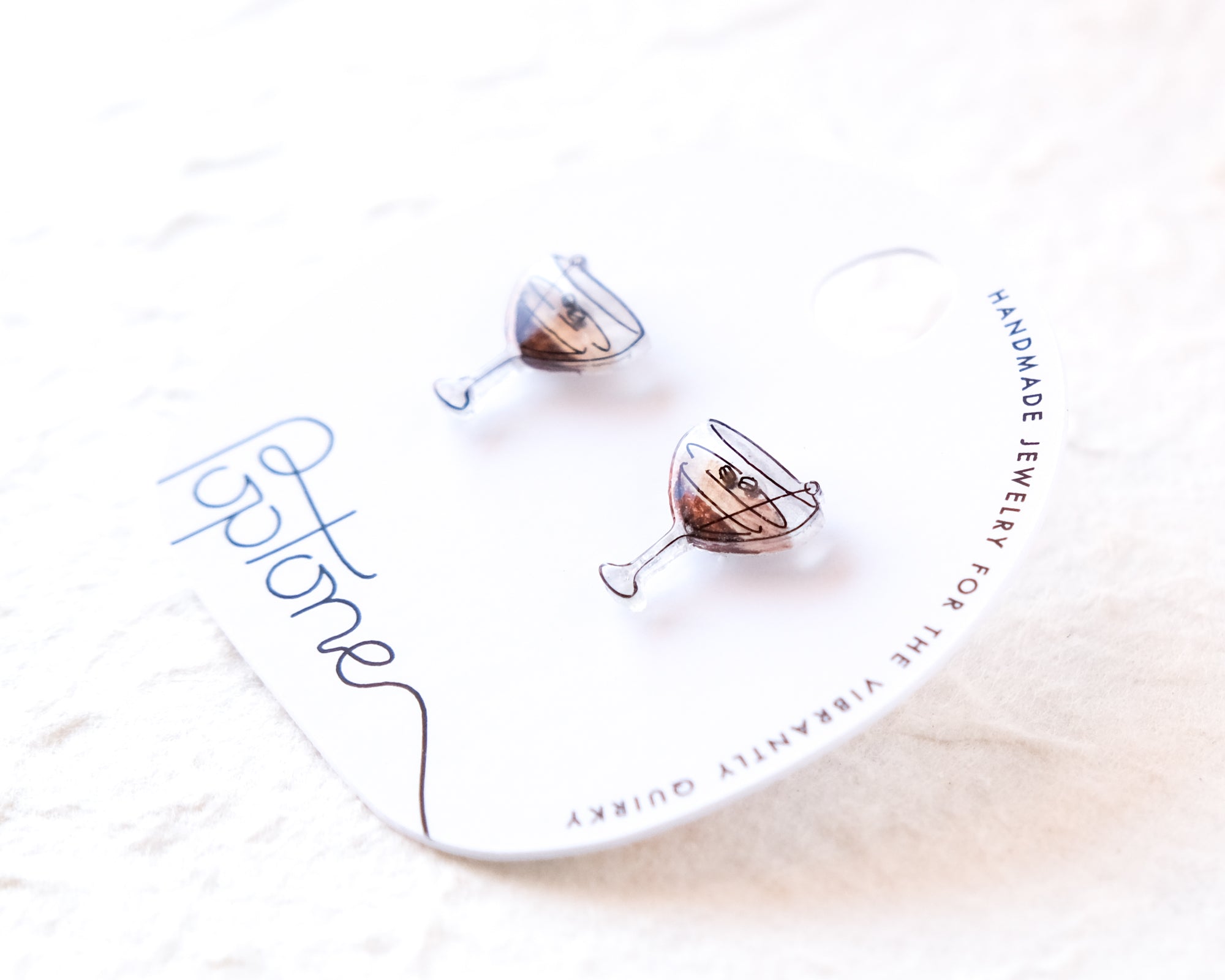 a pair of earrings with a design resembling a wine glass, placed on a white background.