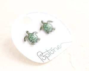 a pair of sea turtle earrings sitting on top of a white plate