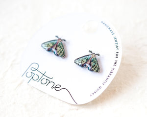 a pair of earrings with butterfly designs, placed on a white circular card with text and graphics.