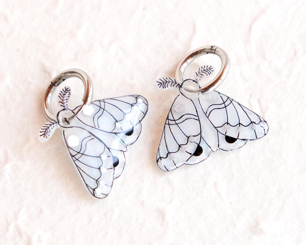 two butterfly-shaped charms with intricate designs, placed on a textured surface.