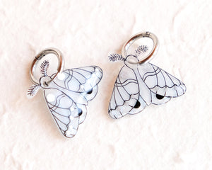 two butterfly-shaped charms with intricate designs, placed on a textured surface.