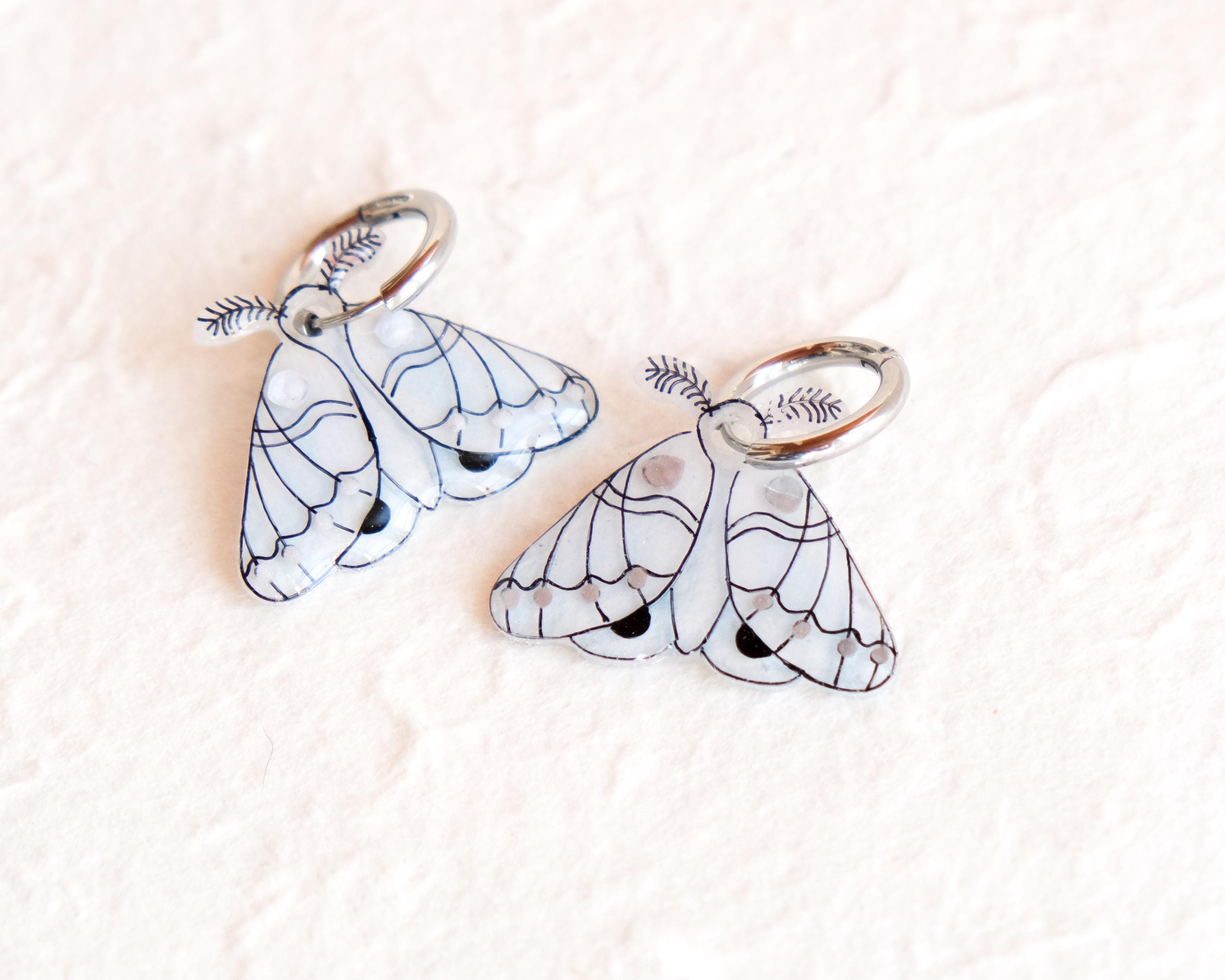 two white butterfly-shaped charms with black outlines and details, placed on a white surface.