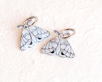 Load image into Gallery viewer, two white butterfly-shaped charms with black outlines and details, placed on a white surface.
