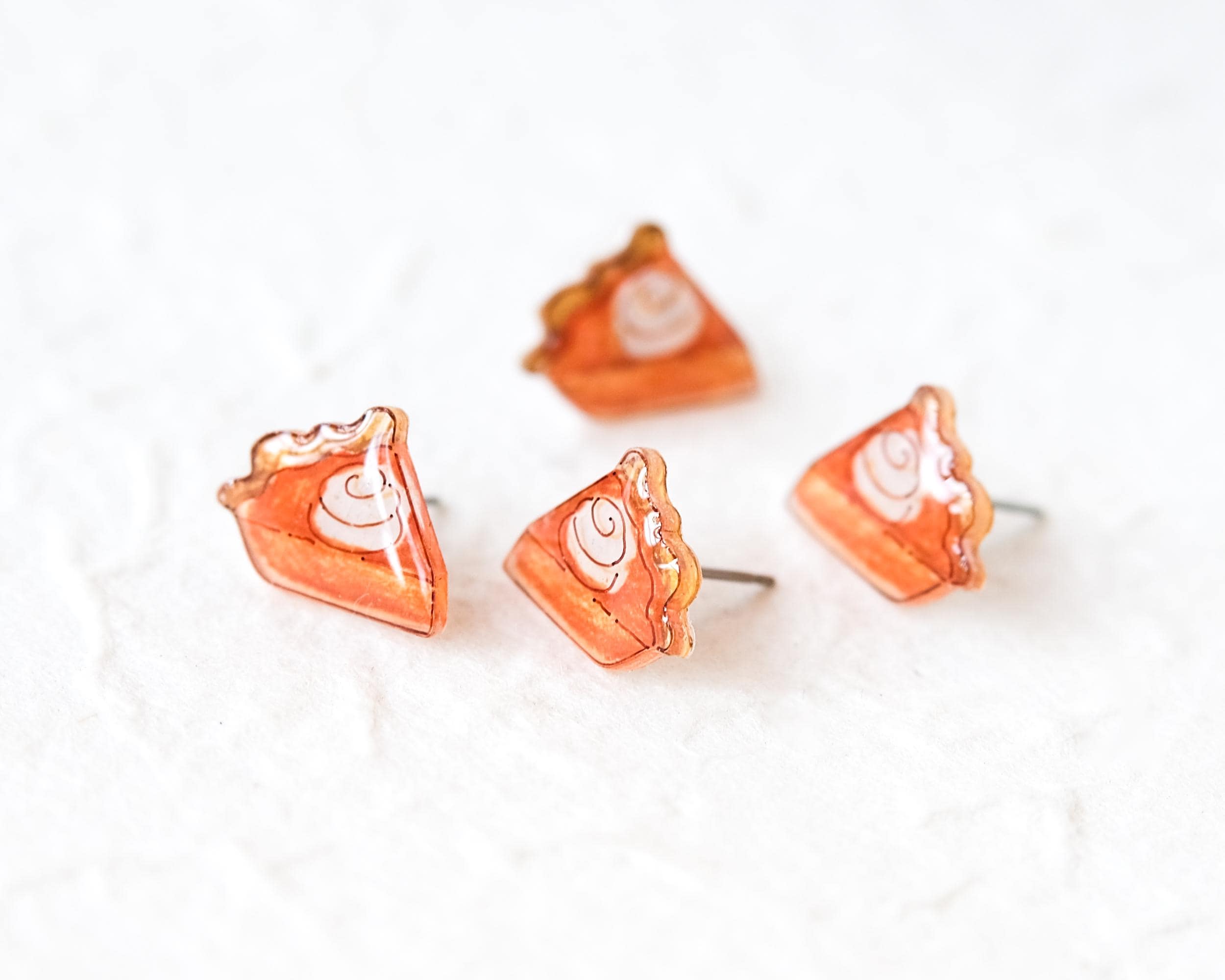 A group of four small, orange-colored earrings with white swirl designs on them, arranged on a white surface.