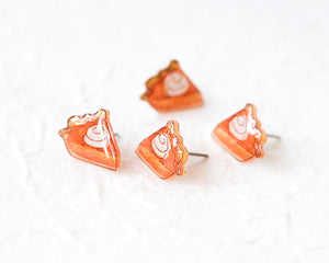 A group of four small, orange-colored earrings with white swirl designs on them, arranged on a white surface.