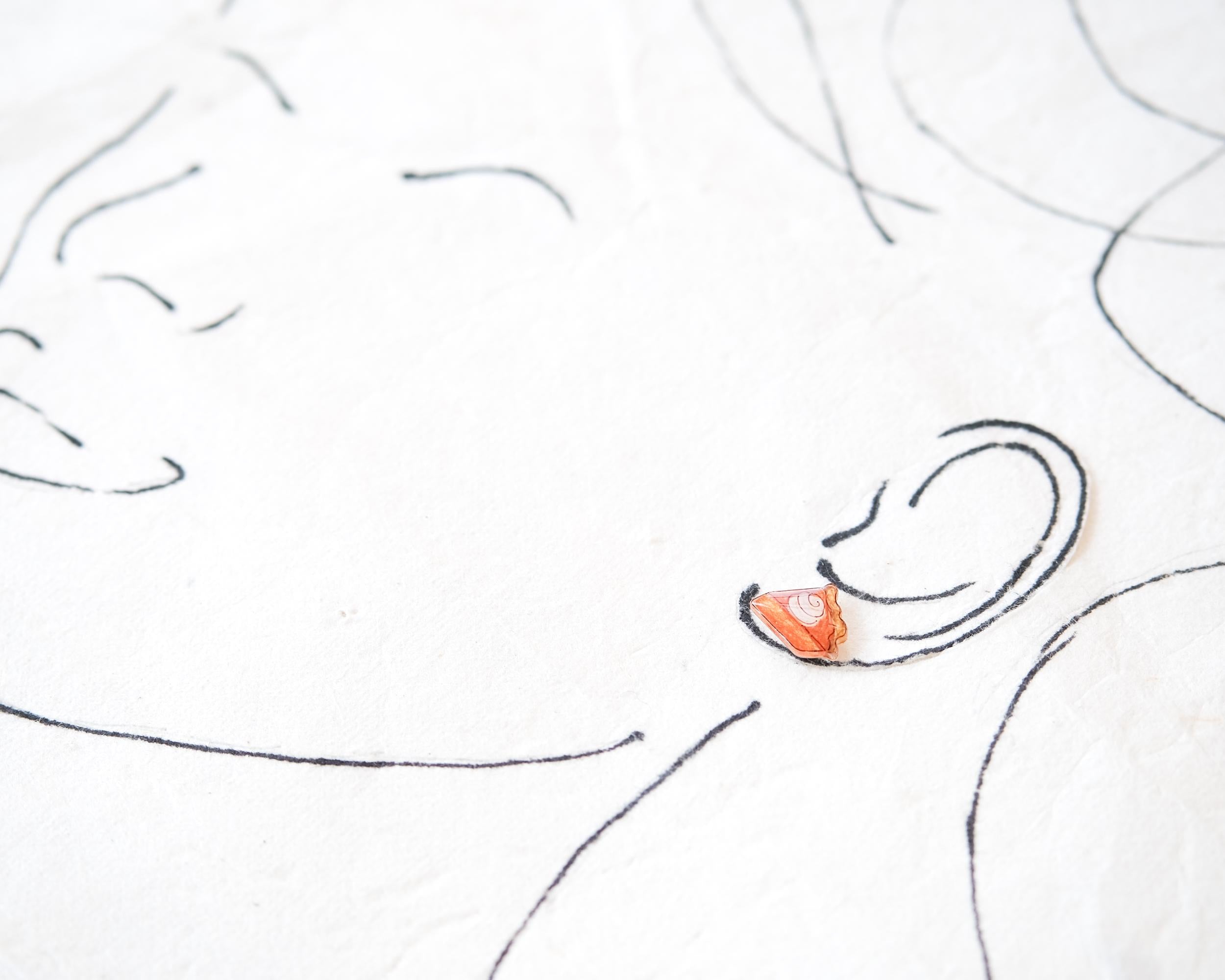 a close-up view of a person's face, with a small orange object, possibly an earring, placed on the right side of the frame.