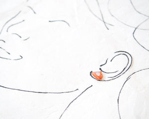 a close-up view of a person's face, with a small orange object, possibly an earring, placed on the right side of the frame.