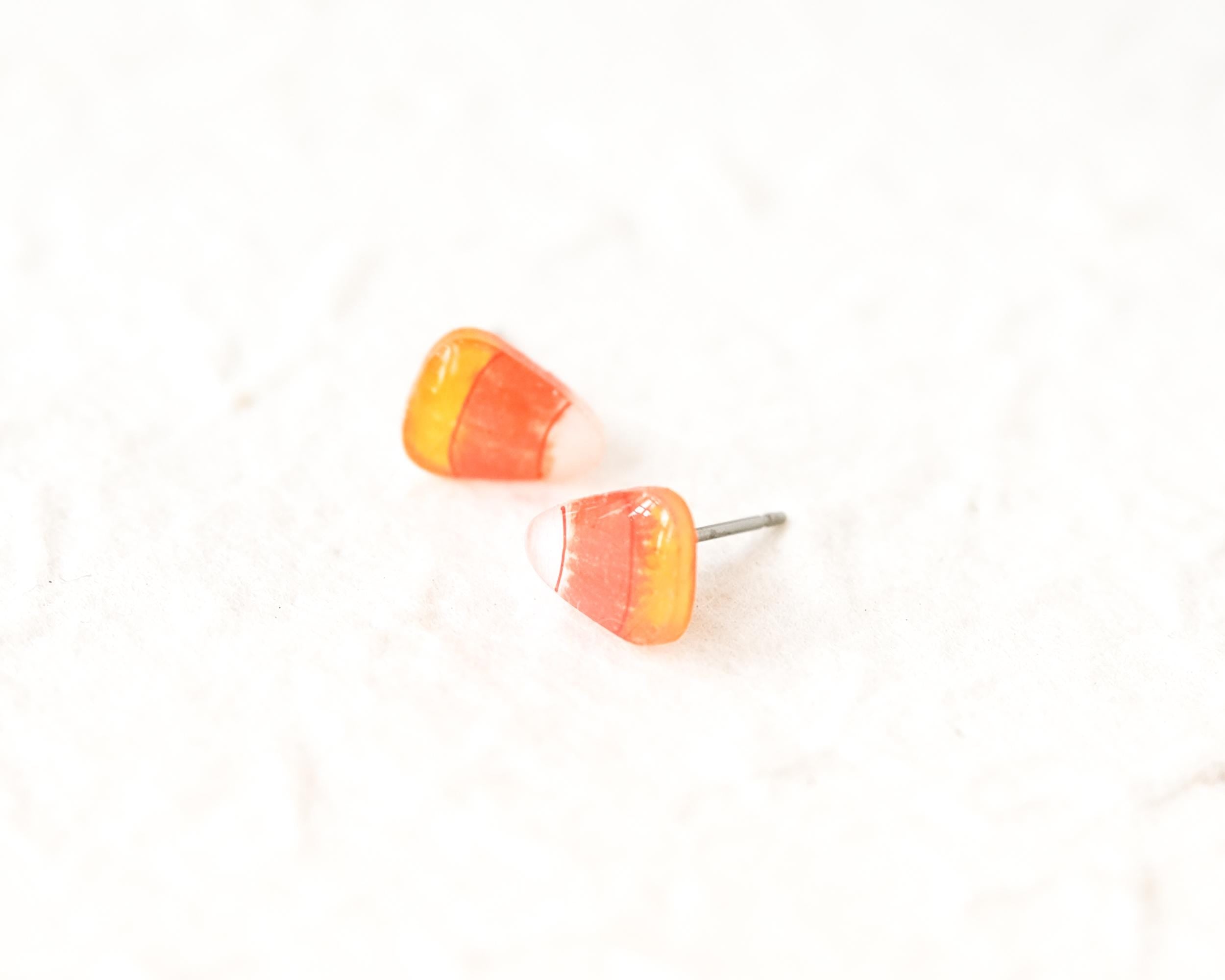 Two candy corn earrings are placed on a white surface.