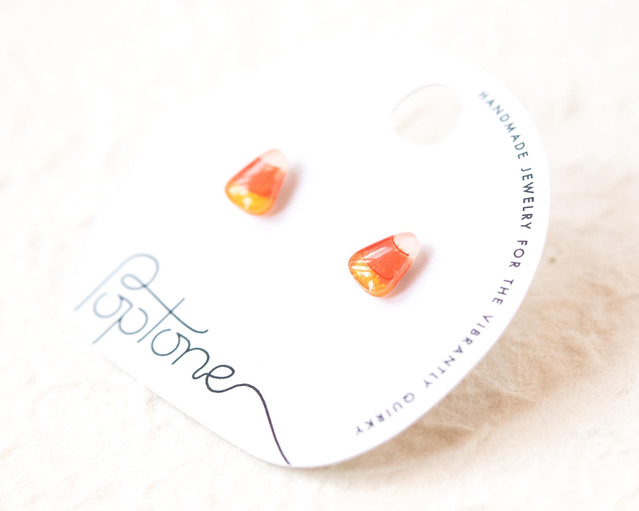 a pair of earrings made of candy, specifically orange and yellow corn candy, placed on a white background.