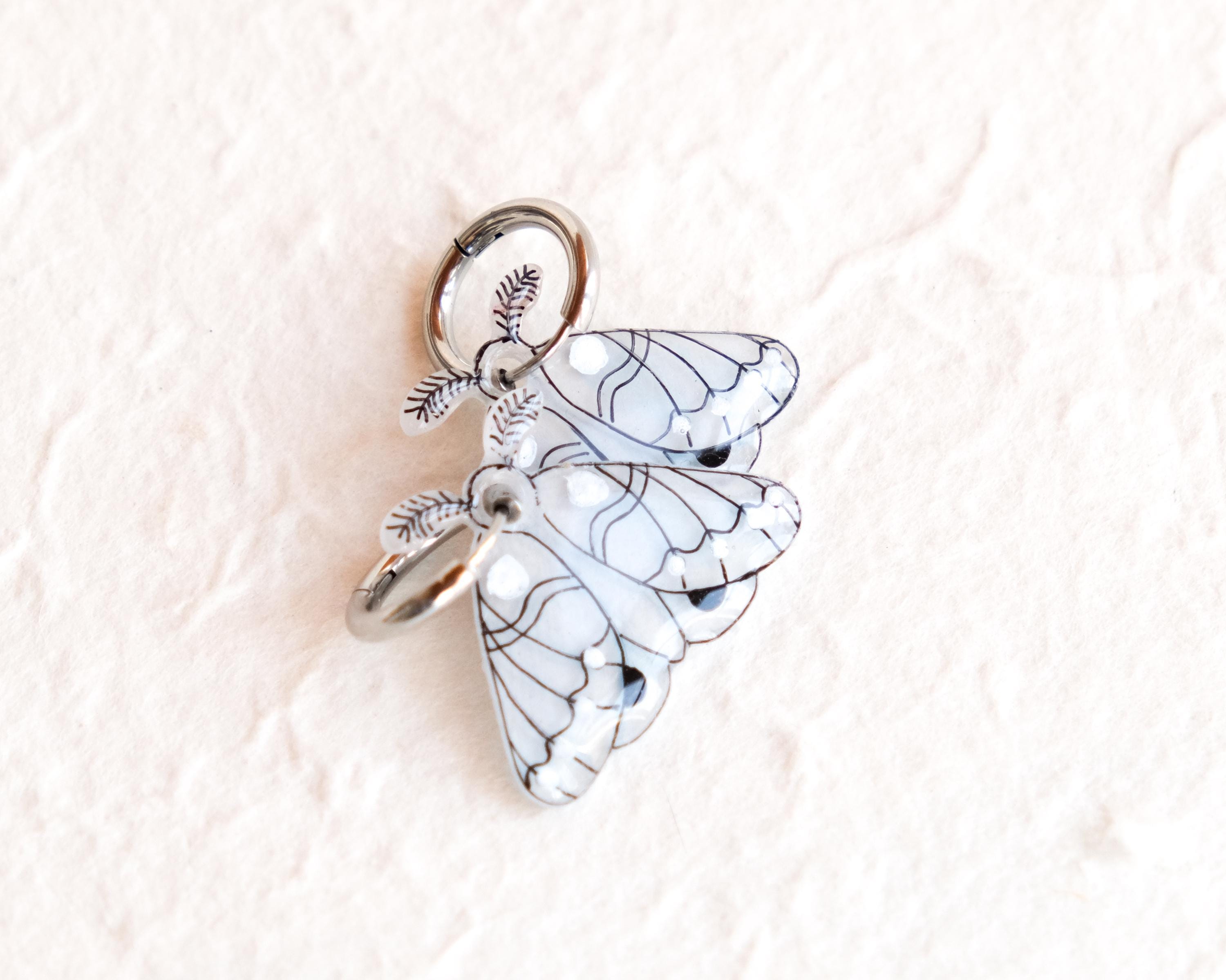 A silver charm in the shape of a butterfly with intricate wing patterns.