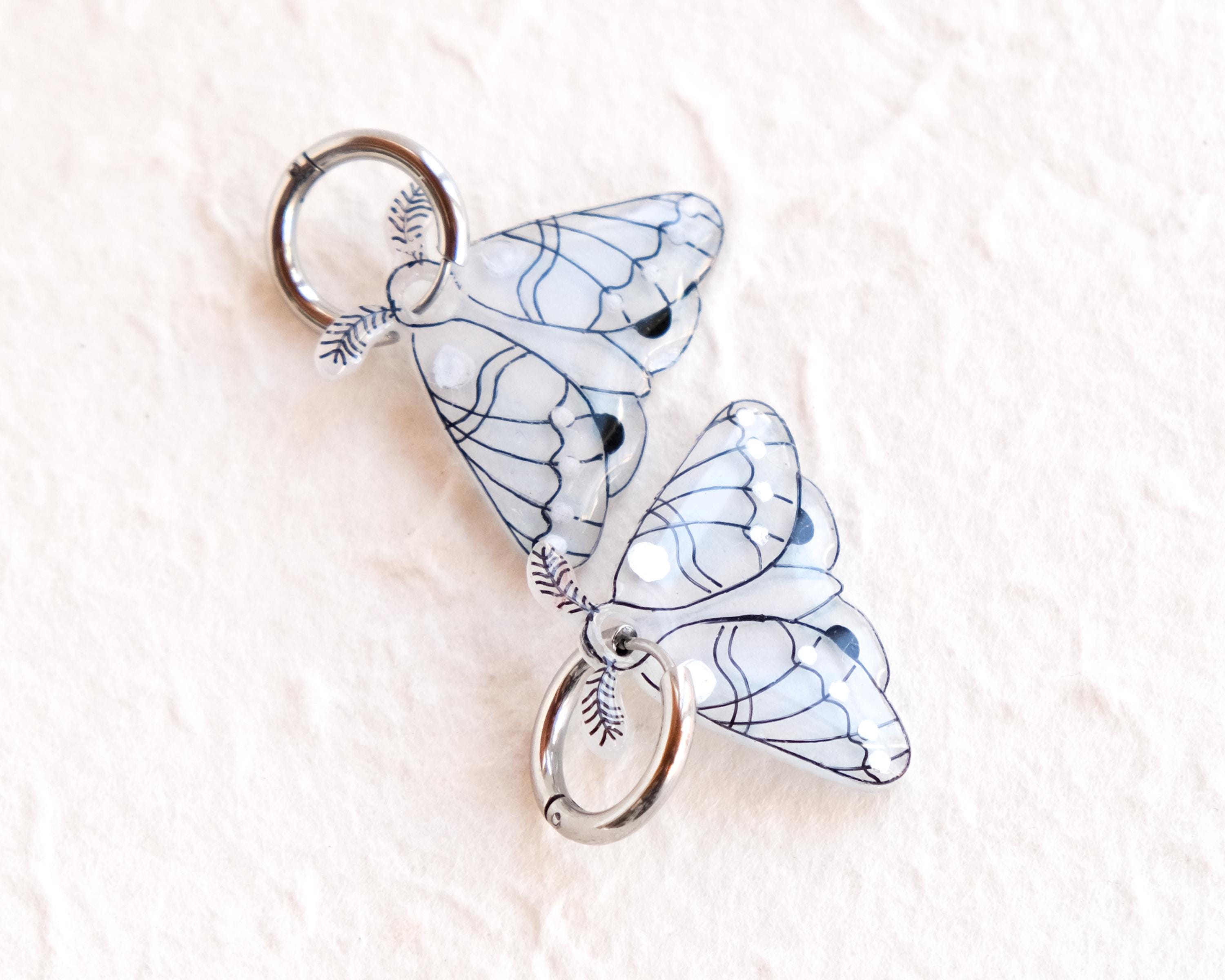 two silver butterfly-shaped charms with intricate designs, hanging from a circular hook.