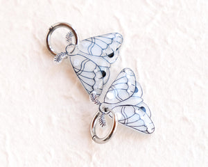 two silver butterfly-shaped charms with intricate designs, hanging from a circular hook.