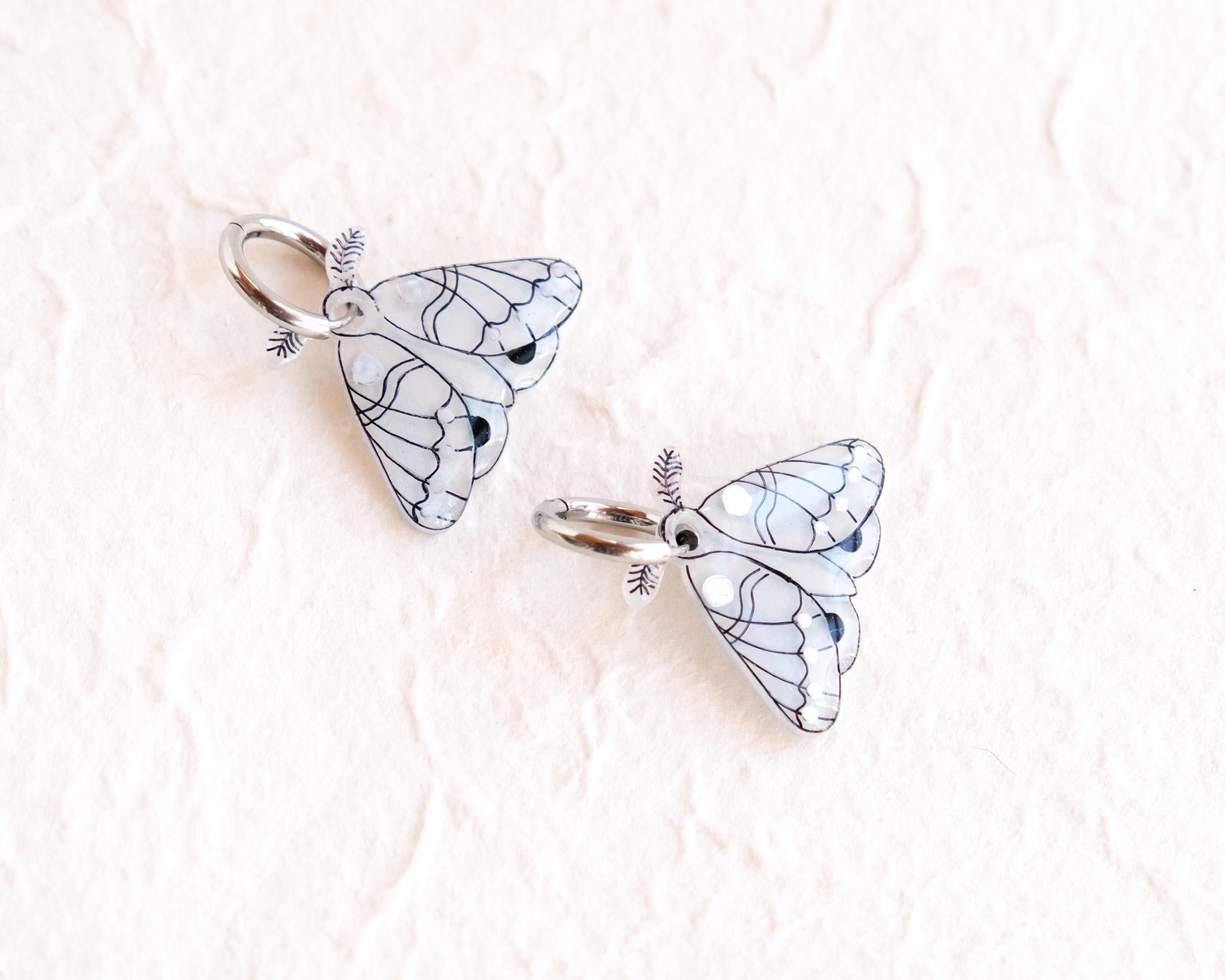 two silver butterfly charms with intricate designs, placed on a white background.