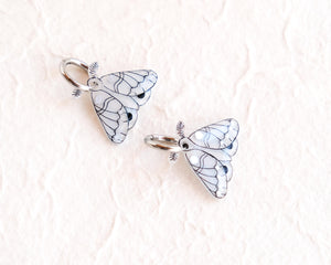 two silver butterfly charms with intricate designs, placed on a white background.