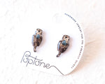 Load image into Gallery viewer, A pair of earrings in the shape of otters, made of a material that resembles wood or stone, are displayed on a white background.
