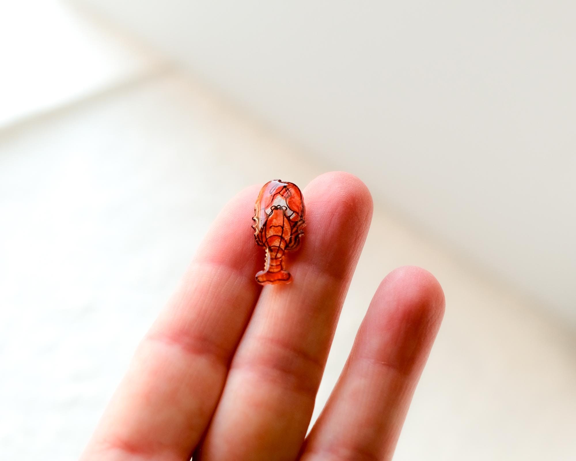 A small, orange lobster pin is being held in a person's hand against a white background.