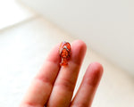 Load image into Gallery viewer, A small, orange lobster pin is being held in a person&#39;s hand against a white background.

