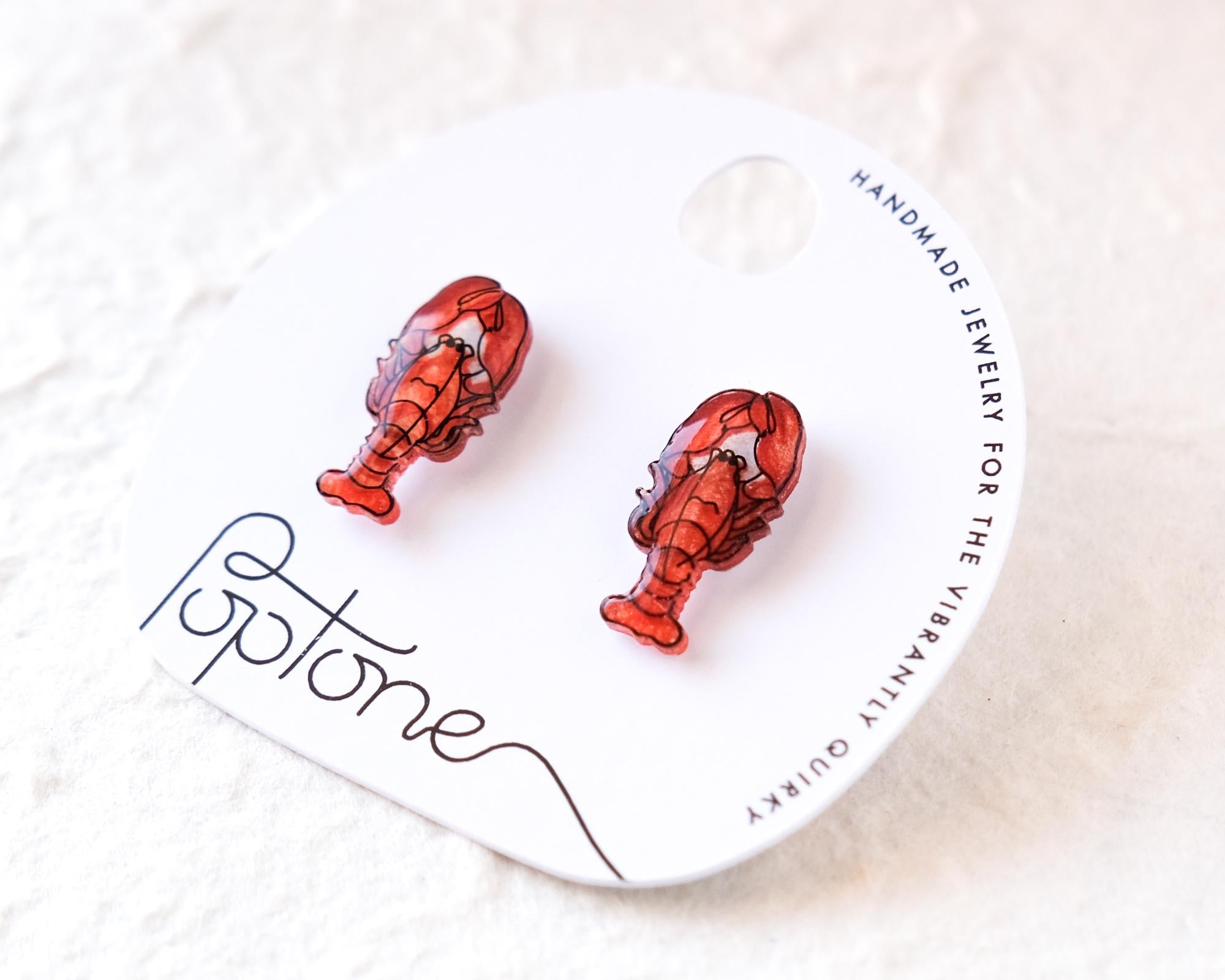 a pair of red lobster earrings displayed on a white circular card with text.